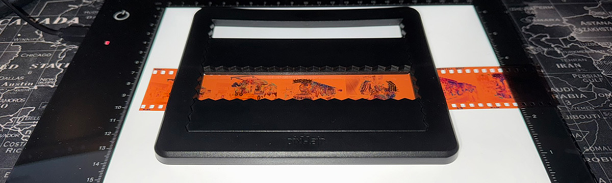 Pixl-latr device holding a strip of 35mm negatives, on a Kaiser Slimlite Plano light table